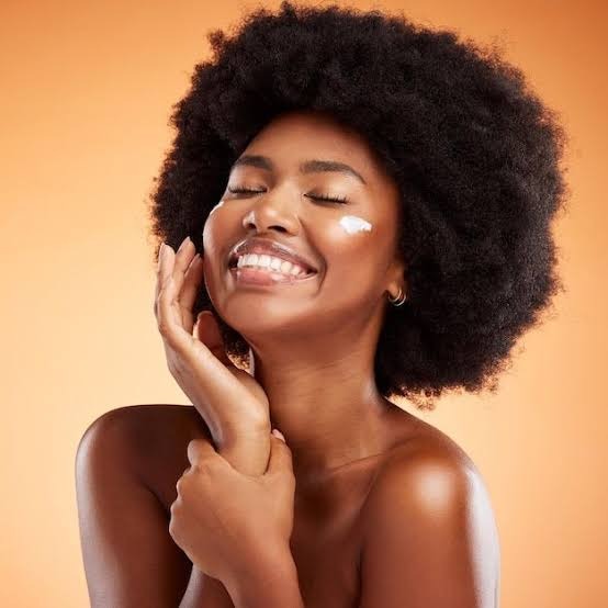 Smiling woman with glowing skin applying skincare cream